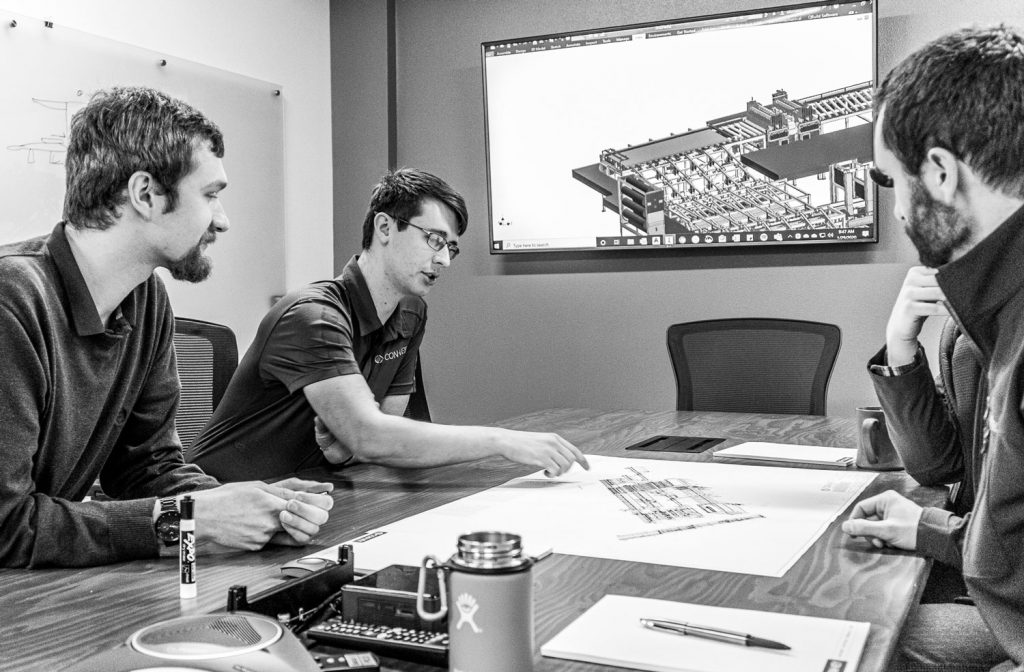 Con-Vey mechanical engineers sales project managers discussing and looking at designed equipment drawing on conference table in office at roseburg oregon