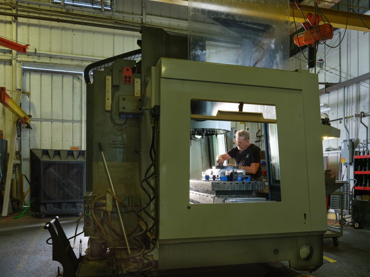 A fabricator inspects a metal part under a hood