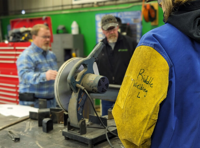 A high school student from the community stands with a chop saw in the Con-Vey shop